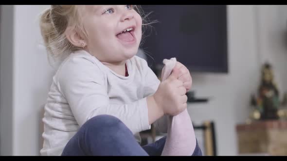 Close-up Portrait of Positive Little Girl Taking Off Pink Sock. Blond Caucasian Child Enjoying Free alt