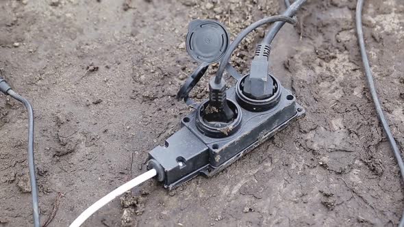 An Extension Cord with a Plug is Lying on Damp Ground alt