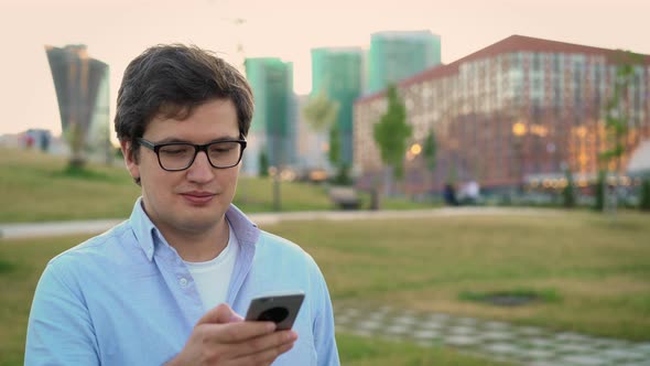 Portrait of Adult Man Using Mobile Phone on Background of Park Lawn