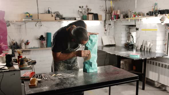Male artisan artist sculptor wipes the product, puts things in order in the workshop alt