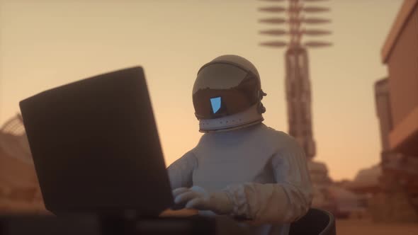 Astronaut in the Space Suit Works on a Laptop in a Space Colony on One of the Planets alt