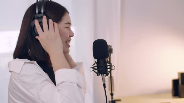 Beautiful Young Asian woman influencer talking into a microphone while recording a podcast.