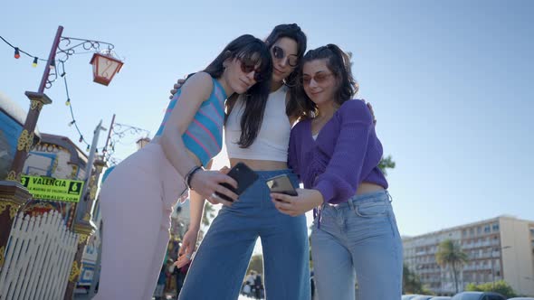 Young Women in Sunglasses Take Selfies with Phones Ground View alt