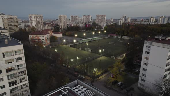 Aerial View of Football Soccer Fields in City Park Against Urban Landscape in the Evening alt