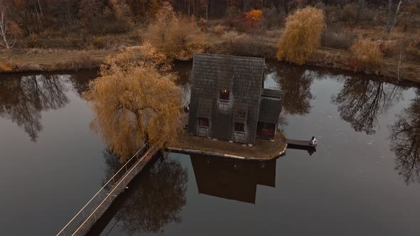 Aerial Footage From Drone of Woman Traveler Standing By Old Wooden House Chalet By Lake Among Trees alt