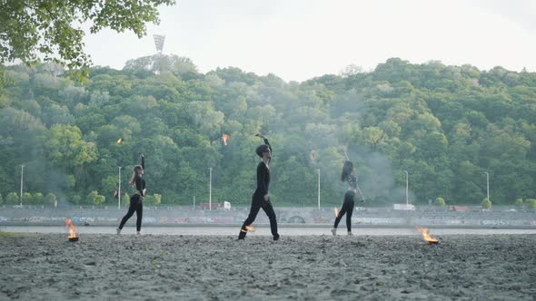 Young Slim Man and Two Beautiful Women Simultaneously Perform Show with Flame alt