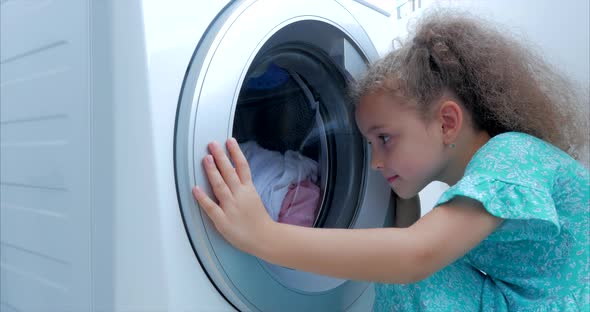 Close Up Cute Child Looks Inside the Washing Machine. Cylinder Spinning Machine. Concept Laundry alt