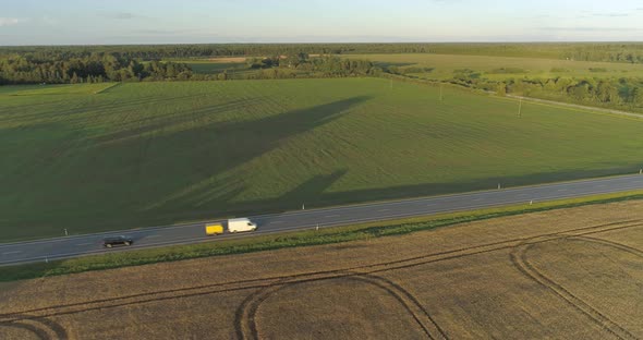 Aerial View of Cars and Cargo Truck Driving on Highway in Countryside at Sunset alt