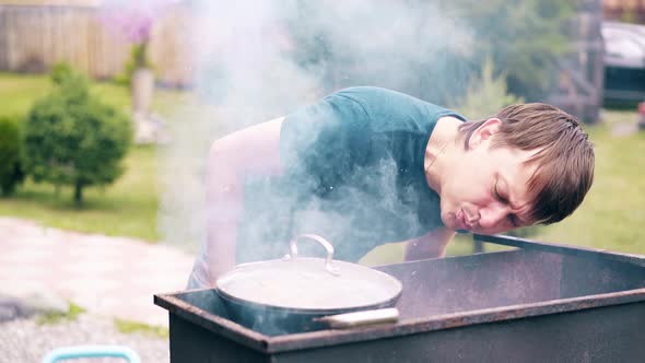 CU, Slow Motion: Young Man Makes Pilaf, in a Cauldron, on a Grill, on an Open Fire alt