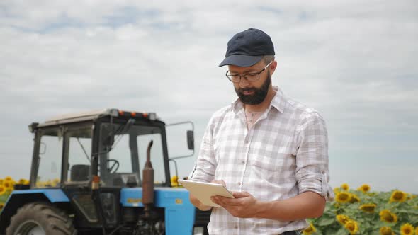 Farmer Uses Tablet in the Field Near the Tractor alt