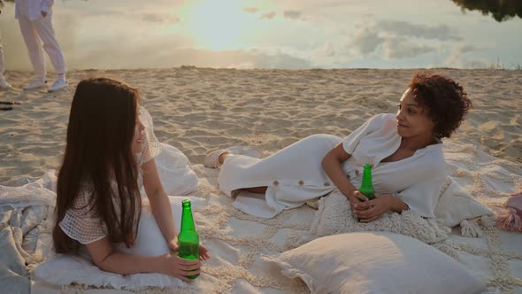 Young Girls Chatting and Drinking While Laying on a Beach at the Sunset