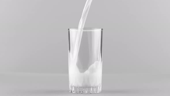 Milk Pouring Into Glass Close Up Isolated on Light Grey Background alt