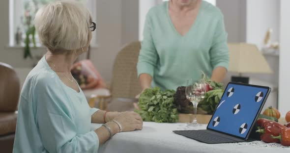 Side View of Slim Senior Woman Reading Recipe From Webpage on Blue Screen Laptop As Unrecognizable alt