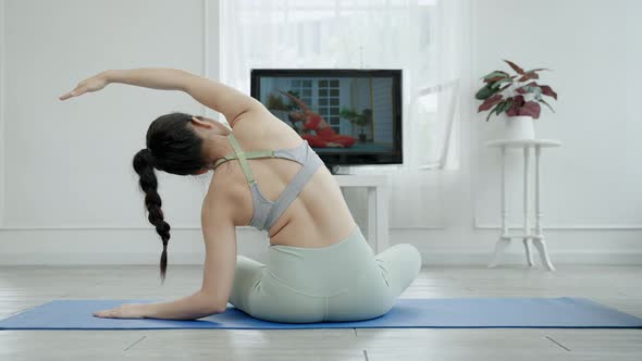 The back of an Asian woman practicing yoga online through TV, health concept.