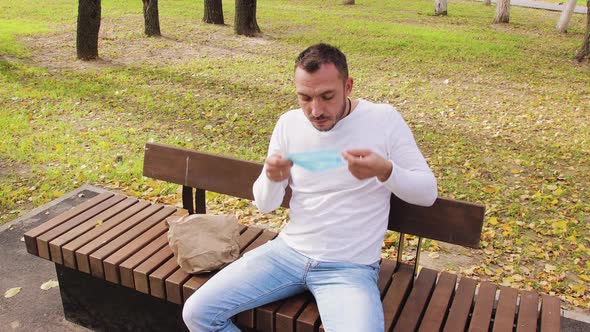 Handsome Business Young Man Sitting on a Bench Puts on a Medical Mask alt