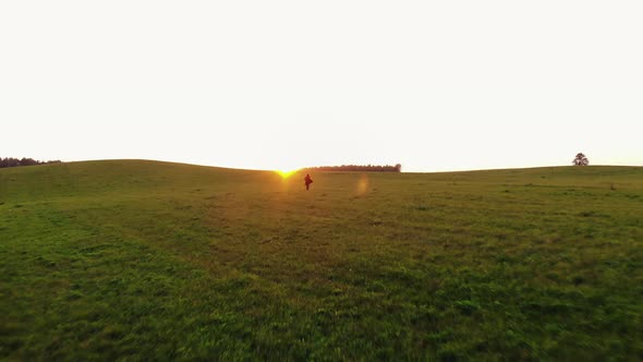Shooting From Drone of a Young Girl Running Through Green Hilly Meadows Against the Backdrop of a