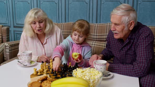 Senior Couple Grandfather Grandmother Resting on Sofa Playing Chess with Granddaughter Child Kid alt