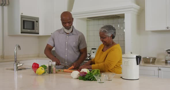 African american senior couple chopping vegetables together in the kitchen at home alt