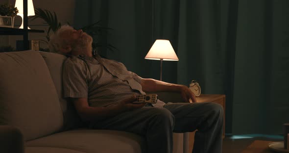 Senior man sitting on the sofa and sleeping while watching TV at night