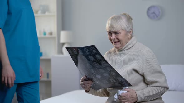 Nurse Supporting Crying Old Woman Looking at Brain Roentgen, Fatal Diagnosis alt