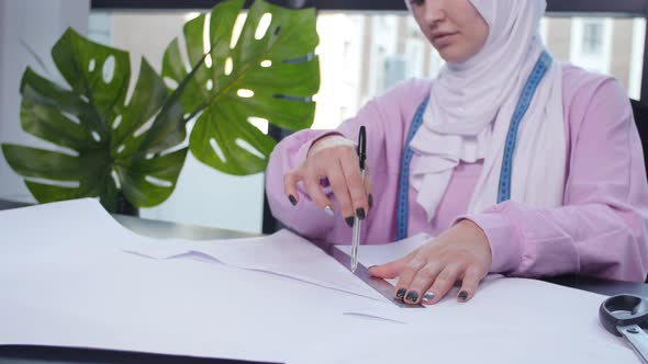 Small Business and Hobby Concept. Muslim Woman Fashion Designer Pinning Paper Pattern at the Table alt
