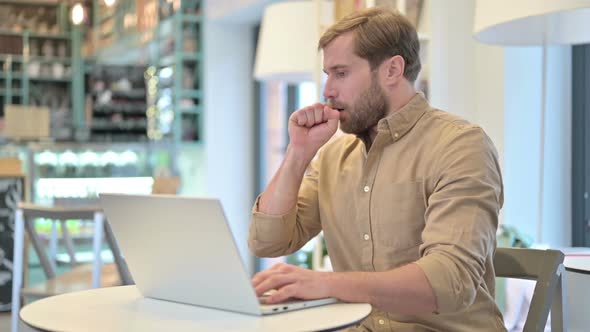 Coughing Young Man Using Laptop in Cafe alt