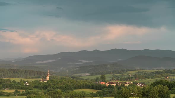 Fog Coming Down from Mountain Range to Village at Sunset,