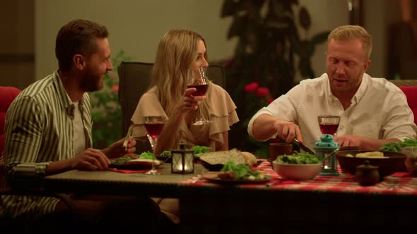 Friends Eating Meal During Dinner. Men and Woman Talking at Dining Table alt