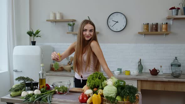 Vegan Girl in Kitchen Adding Lemon Juice To Salad with Raw Vegetables. Weight Loss and Diet Concept alt