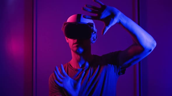 Man in a Virtual Reality Helmet Illuminated in Red and Blue Plays a Game alt
