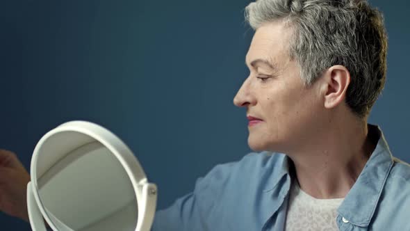 An Elderly Woman Who Cares About Her Appearance Tints Her Eyes While Sitting in Front of a Mirror at