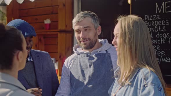 Smiling shop assistant communicate with clients near food booth