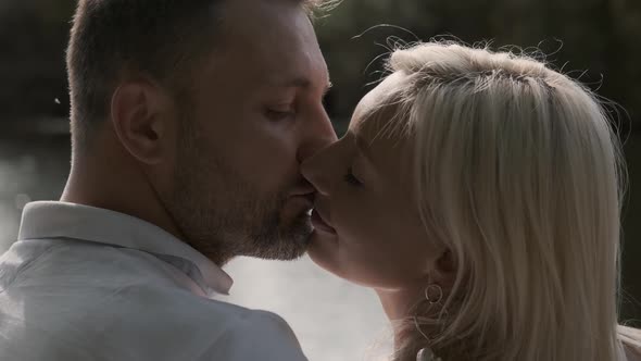 Loving Beautiful Couple Kissing While Sitting on a Pier Near the River. Close-up alt