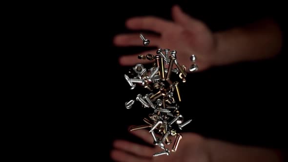 Hands Throw Metal Screws and Nuts of Yellow and Grey Colours