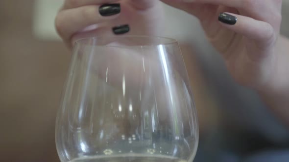 Female Hands Holding Golden Wedding Ring Under the Glass of White Wine alt