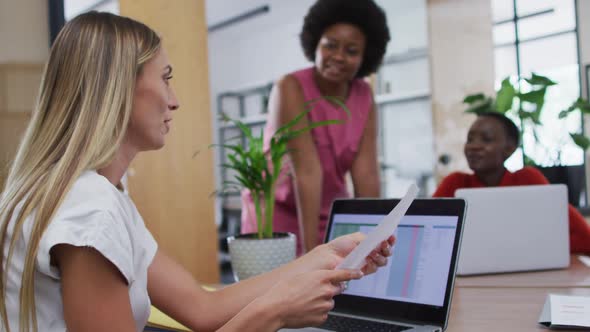 Caucasian woman reading a document to her female office colleagues at office alt