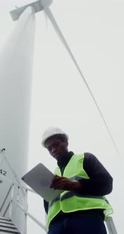 A Man in a Work Uniform is Diagnosing a Wind Turbine Using a Digital Tablet alt