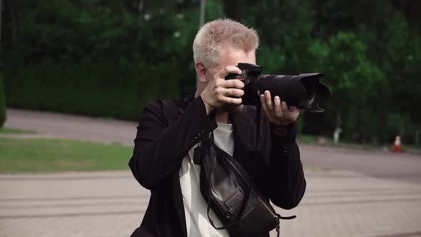 Male Photographer Takes Photos on a Professional Camera Outdoors in Park