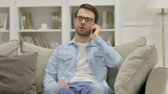 Angry Young Man Talking on Smartphone at Home alt