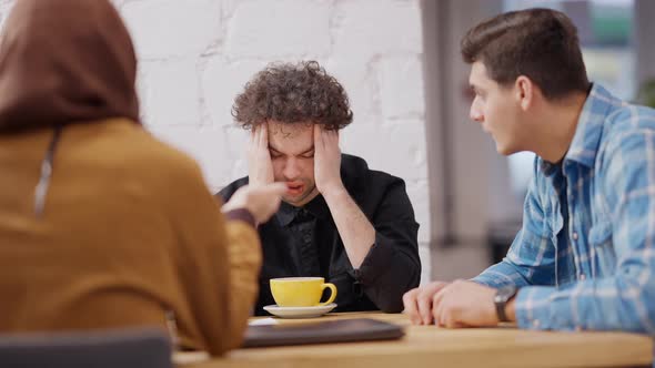 Portrait of Stressed Exhausted Millennial Middle Eastern Man Rubbing Temples As Colleagues Talking alt