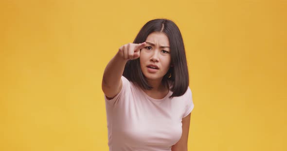 Angry Asian Woman Pointing Finger To Camera, Suspecting and Blaming in Lying, Orange Background alt