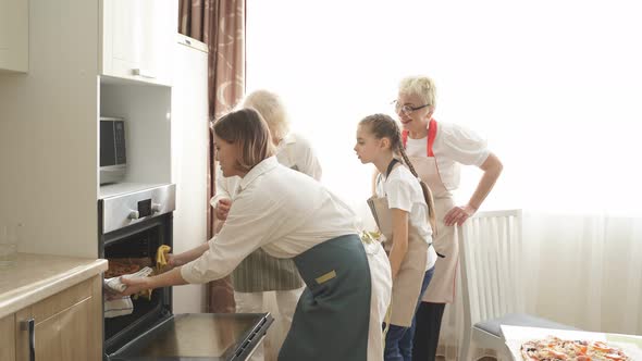 Young Woman Grandmothers and Daughter Take Out a Pizza From an Electric Oven