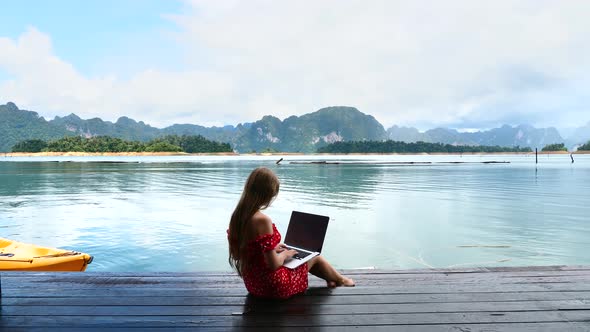 Travel Woman Sitting on Wooden Pier Using Laptop Typing Remote Chatting alt