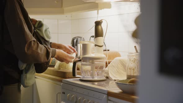 Mother carrying her baby on a sling uses food processor, medium shot pan left alt