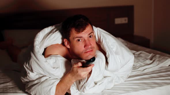 Young Man Under Blanket Lying on Bed and Watching Tv in Evening alt