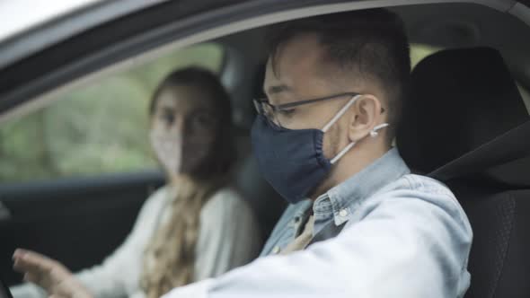Side View of Young Caucasian Man in Covid Face Mask and Eyeglasses Sitting on Driver's Seat and alt