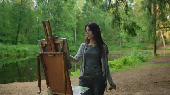 Beautiful Woman Artist Paints a Landscape in a Park Near a Pond alt