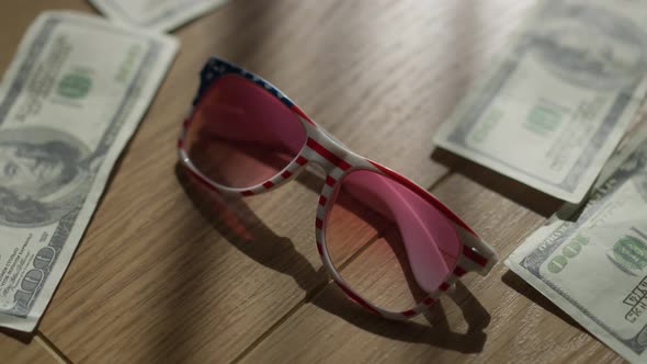 Closeup Stars and Stripes Sunglasses on Wooden Table with Dollars Falling alt
