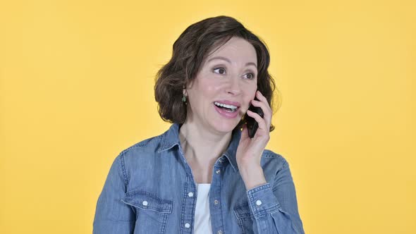 Old Woman Talking on Smartphone on Yellow Background  alt