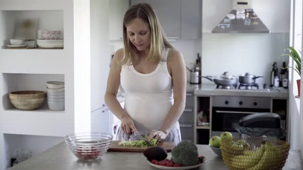 Smiling Future Mother Cutting Salad on Kitchen Table alt